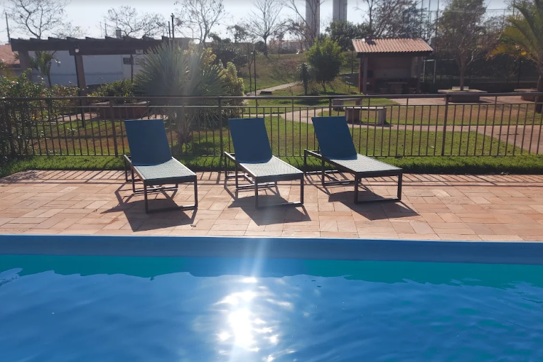 Piscina do condomínio com espreguiçadeiras e área verde ao fundo