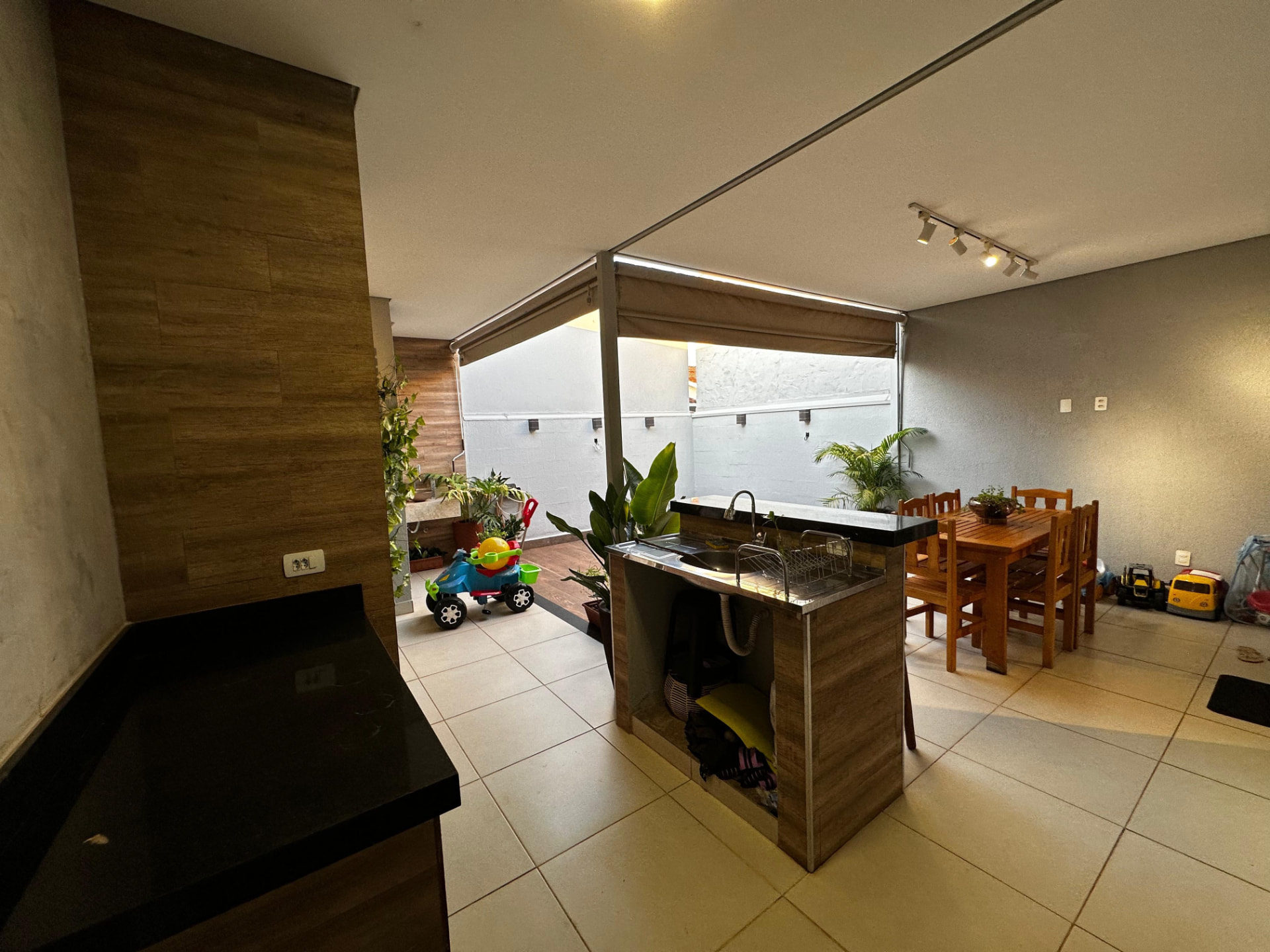 Área gourmet coberta com pia, bancada e mesa de madeira